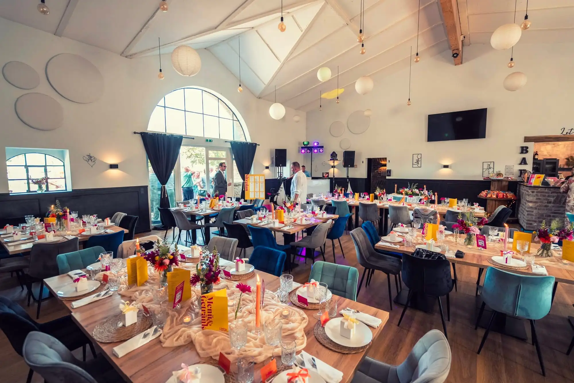 Rundum eingedeckte Tafeln in Gelb, Pink und Orange im hellen Saal
