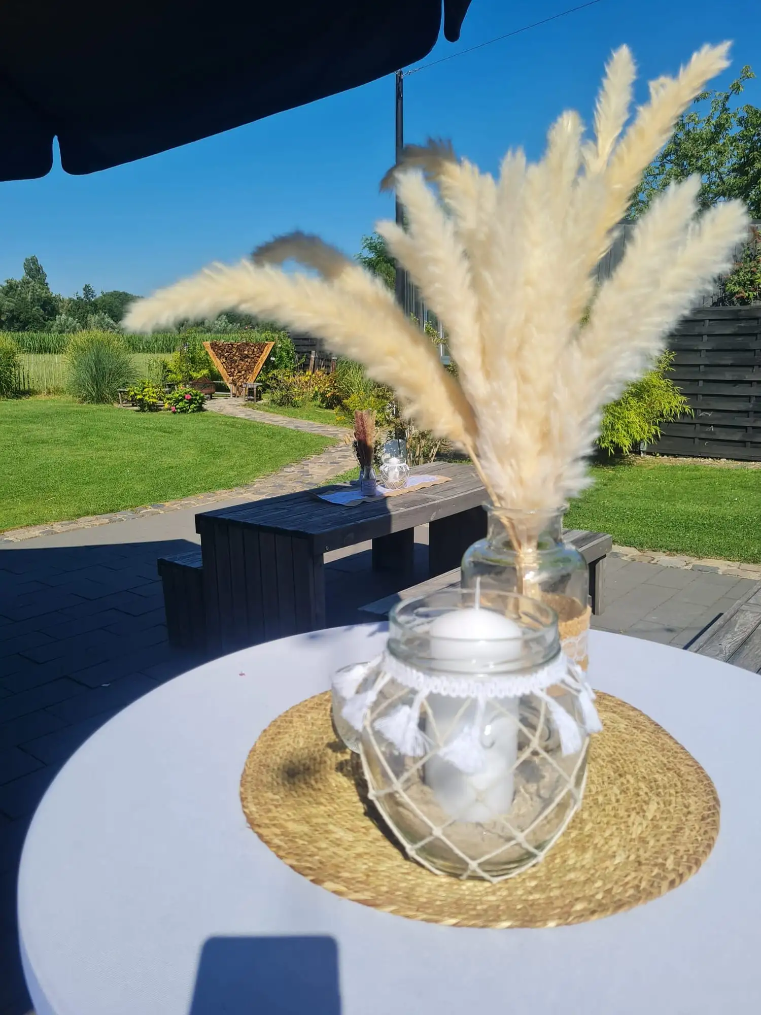 Stehtisch mit Pampasgras in der Glasvase und einem Windlicht, dahinter der sonnige Garten