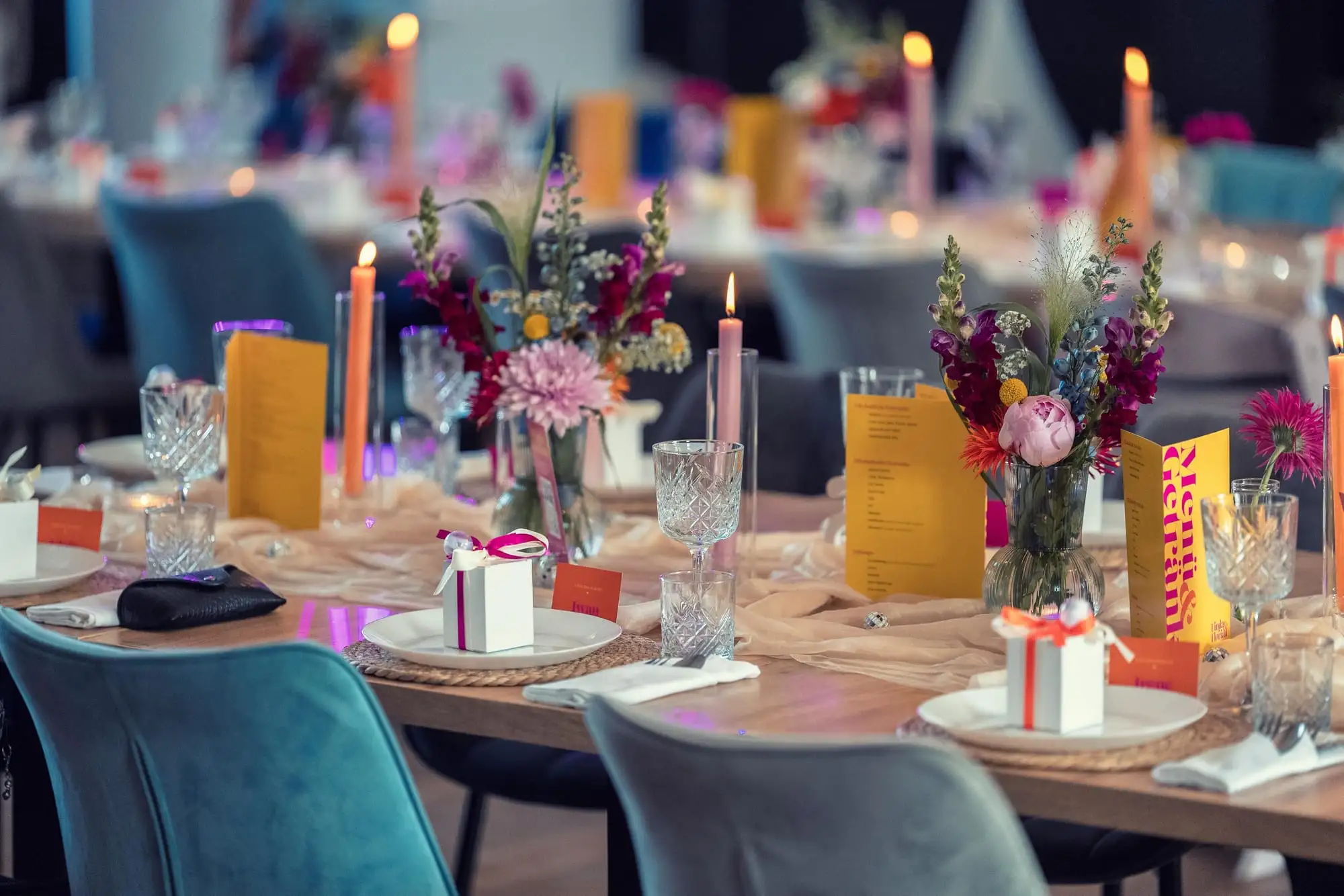 Lange Tafel mit gelben Menükarten, hohen Kerzen und Blumensträußen in Pink und Rot