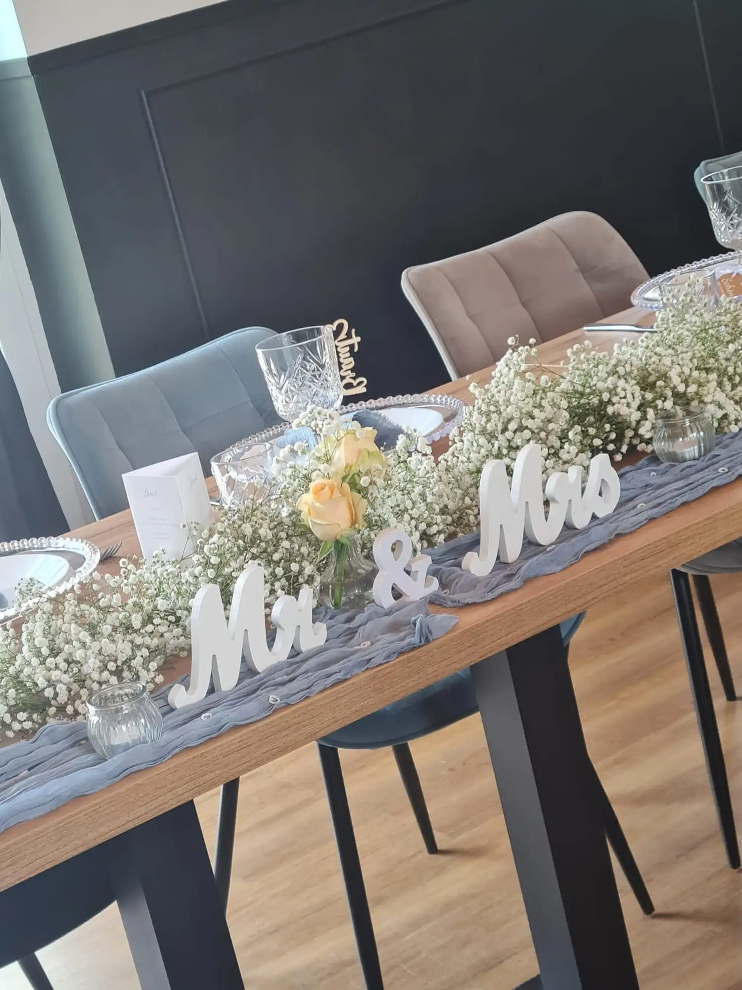 Schriftzug „Mr & Mrs“ zwischen Schleierkraut und Rosen auf dem grauen Tischläufer